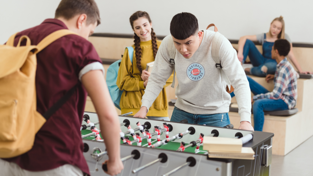 Teens wearing custom football hoodies playing foosball